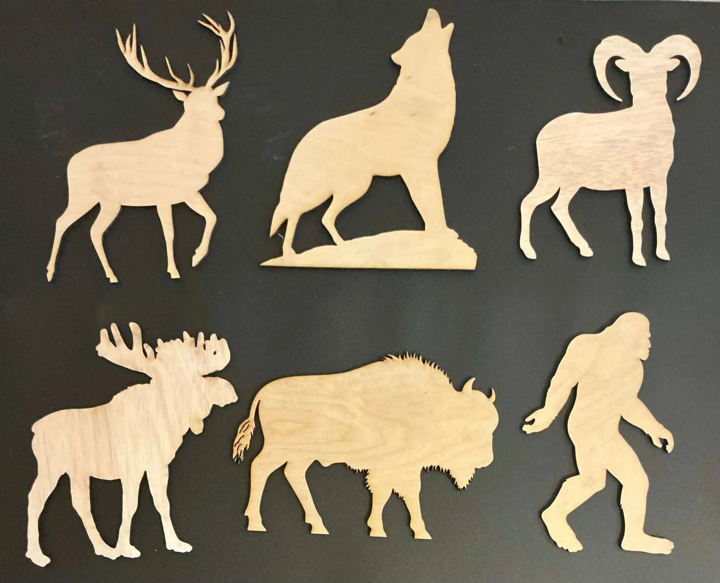 Set of wooden animal cutouts including a deer, wolf, ram, moose, bison, and Bigfoot on a black background.