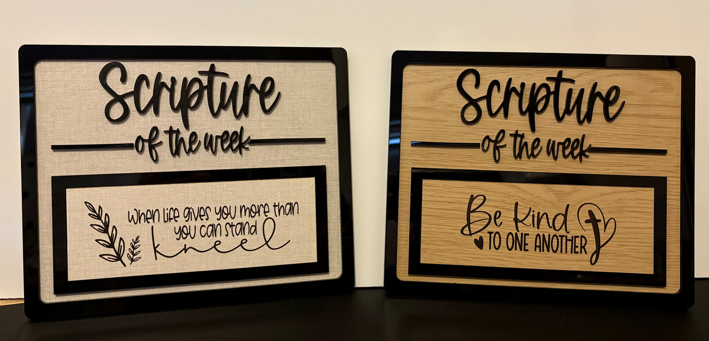 Two wooden signs with 'Scripture of the week' text on a dark surface.