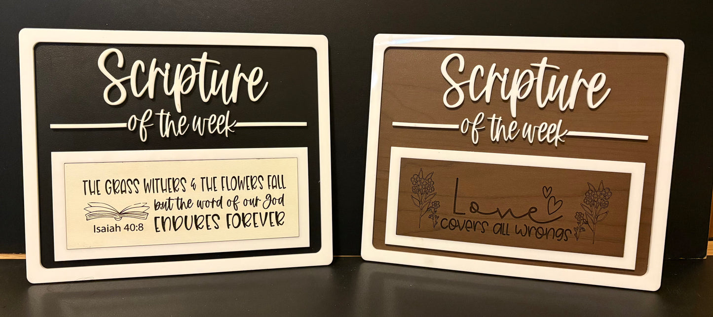 Two wooden signs with 'Scripture of the week' text on a dark surface