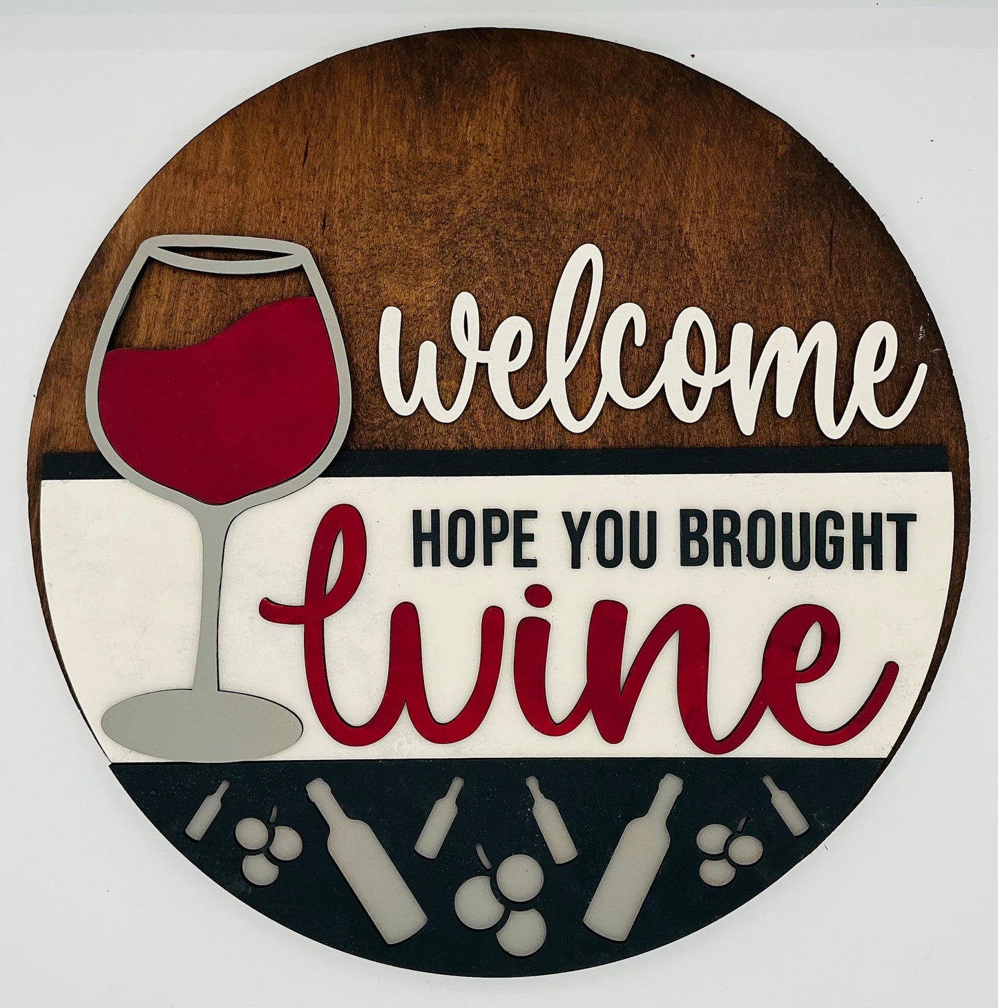 Round wooden sign with a wine glass and text 'Welcome, hope you brought wine' on a white background.