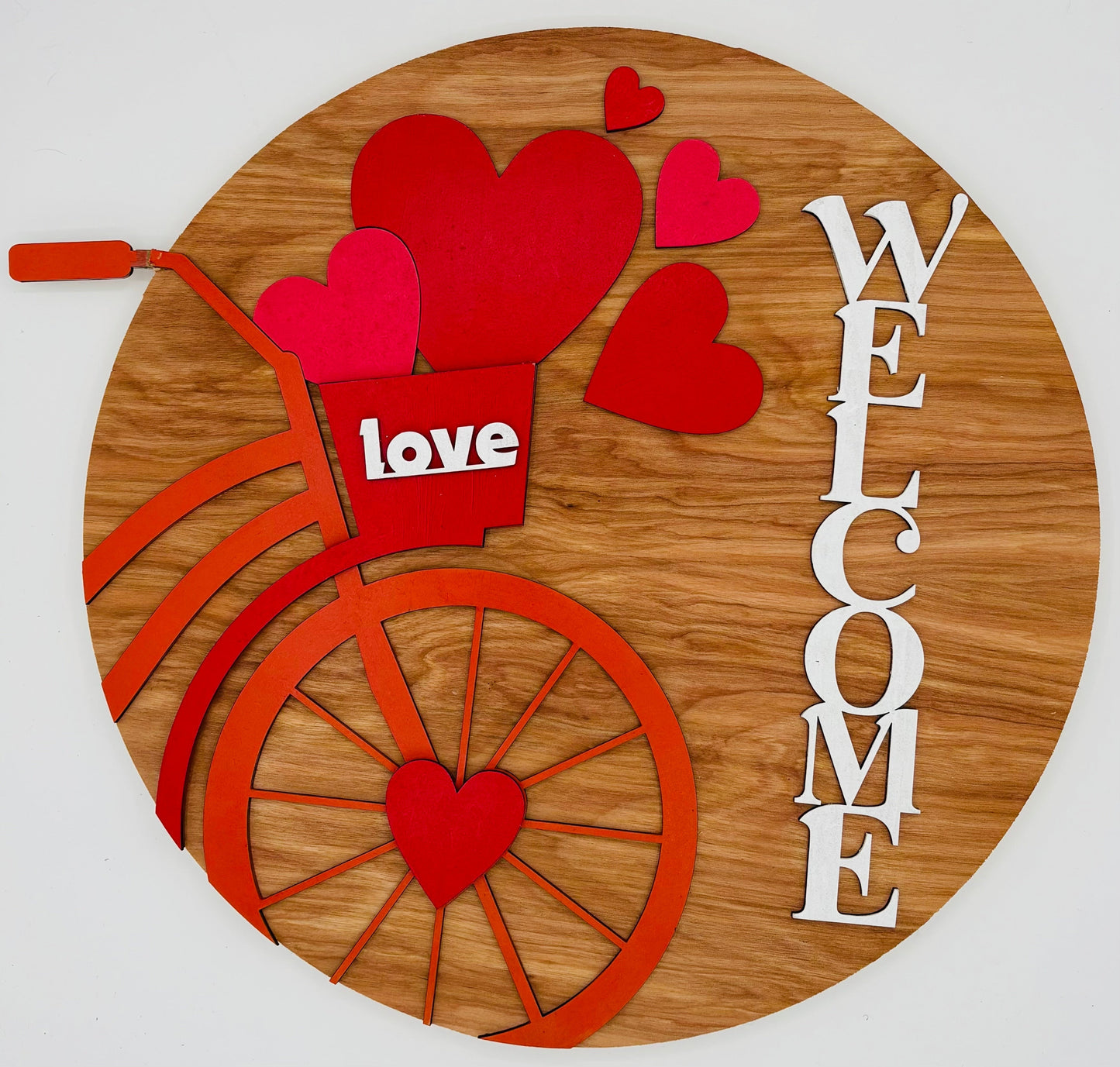 Decorative sign with red hearts, a bicycle, and 'love' and 'welcome' text on a wooden background.
