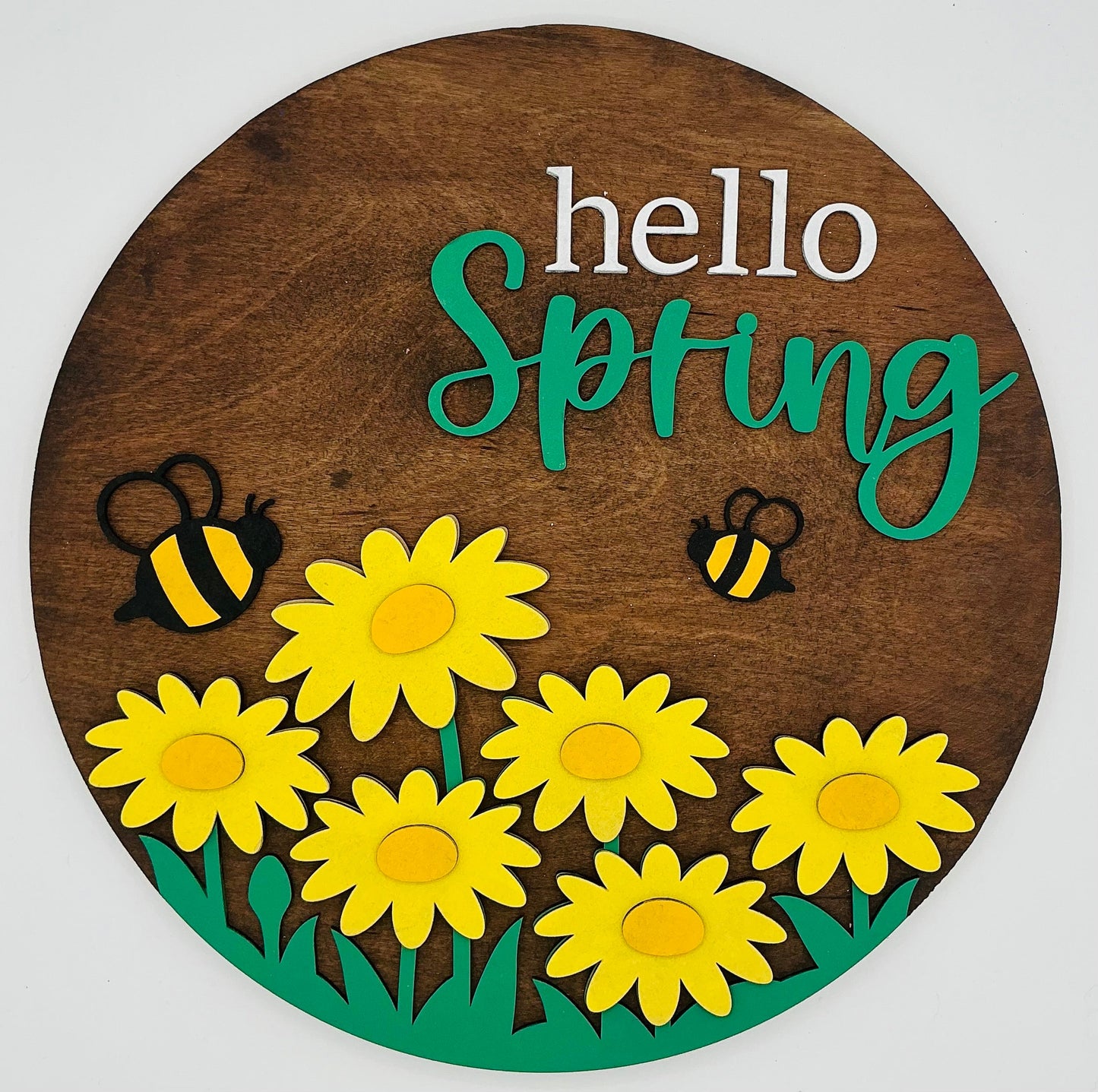 Wooden circular sign with 'hello Spring' text, yellow flowers, and bees on a white background.