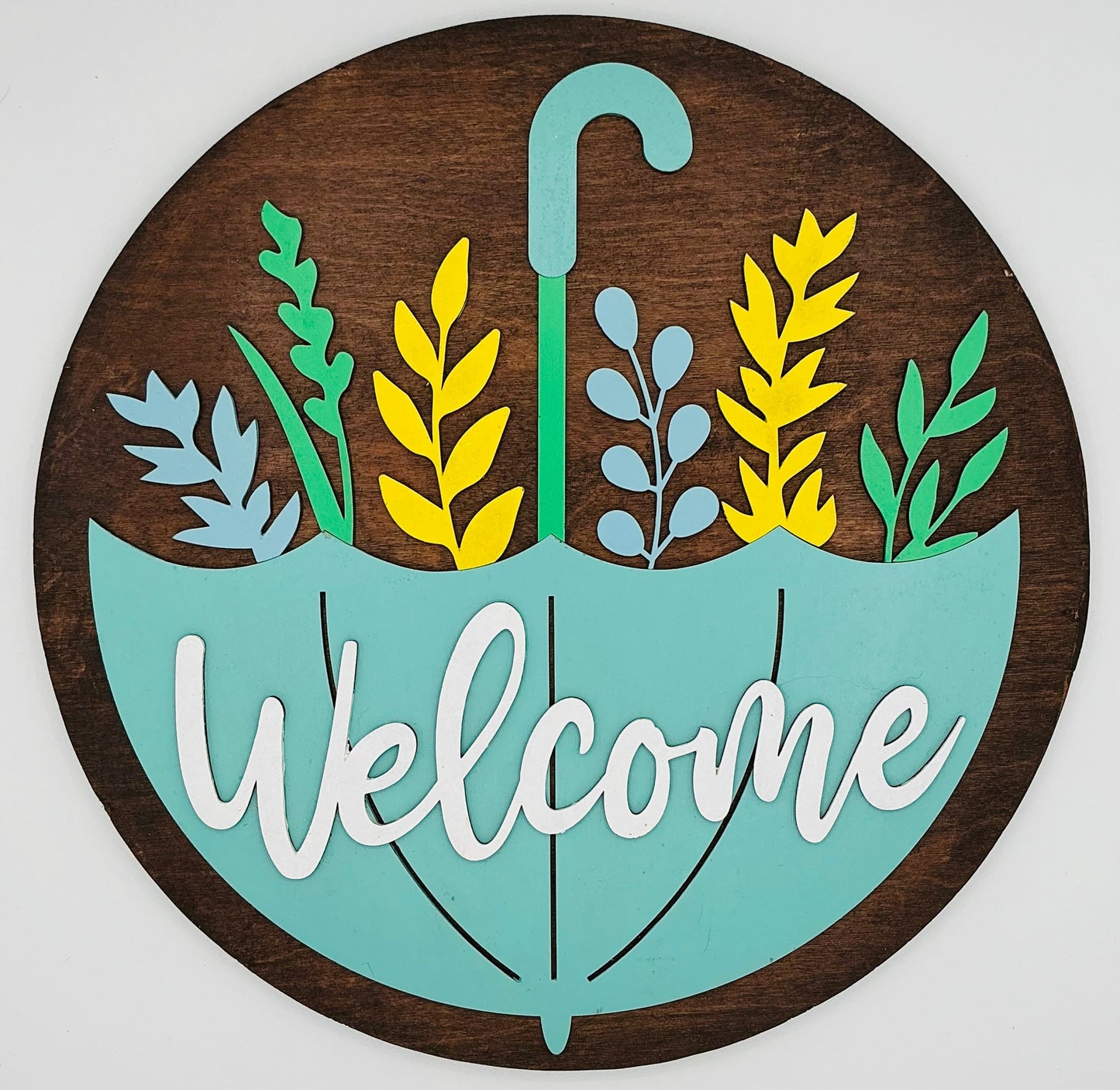 Decorative sign with 'Welcome' text inside a stylized umbrella with leaf designs on a wooden background.