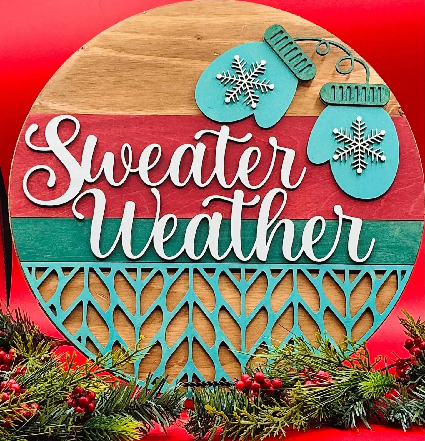 Decorative sign with 'Sweater Weather' text, snowflake designs, and Christmas elements on a red background.