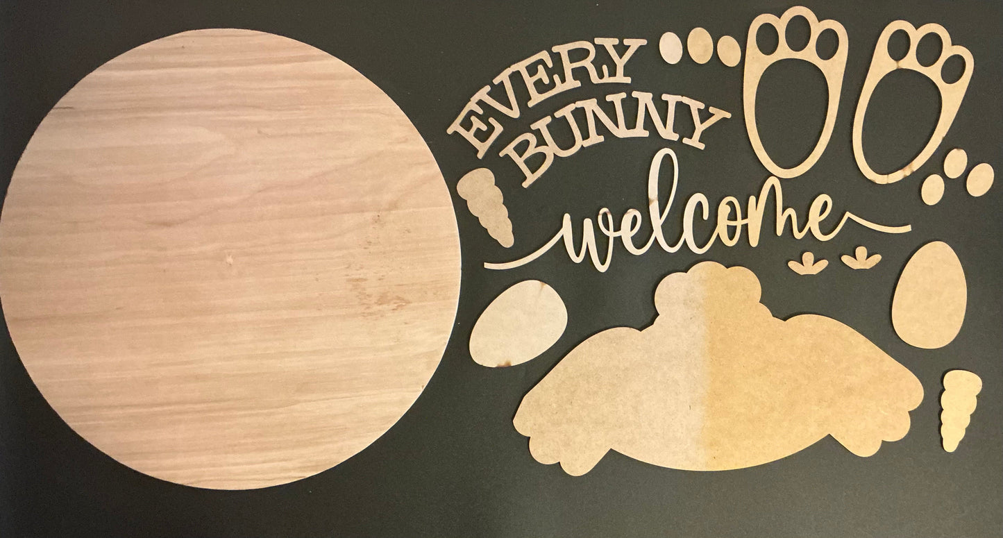 Wooden cutout with 'Every Bunny Welcome' text and bunny footprints on a dark background