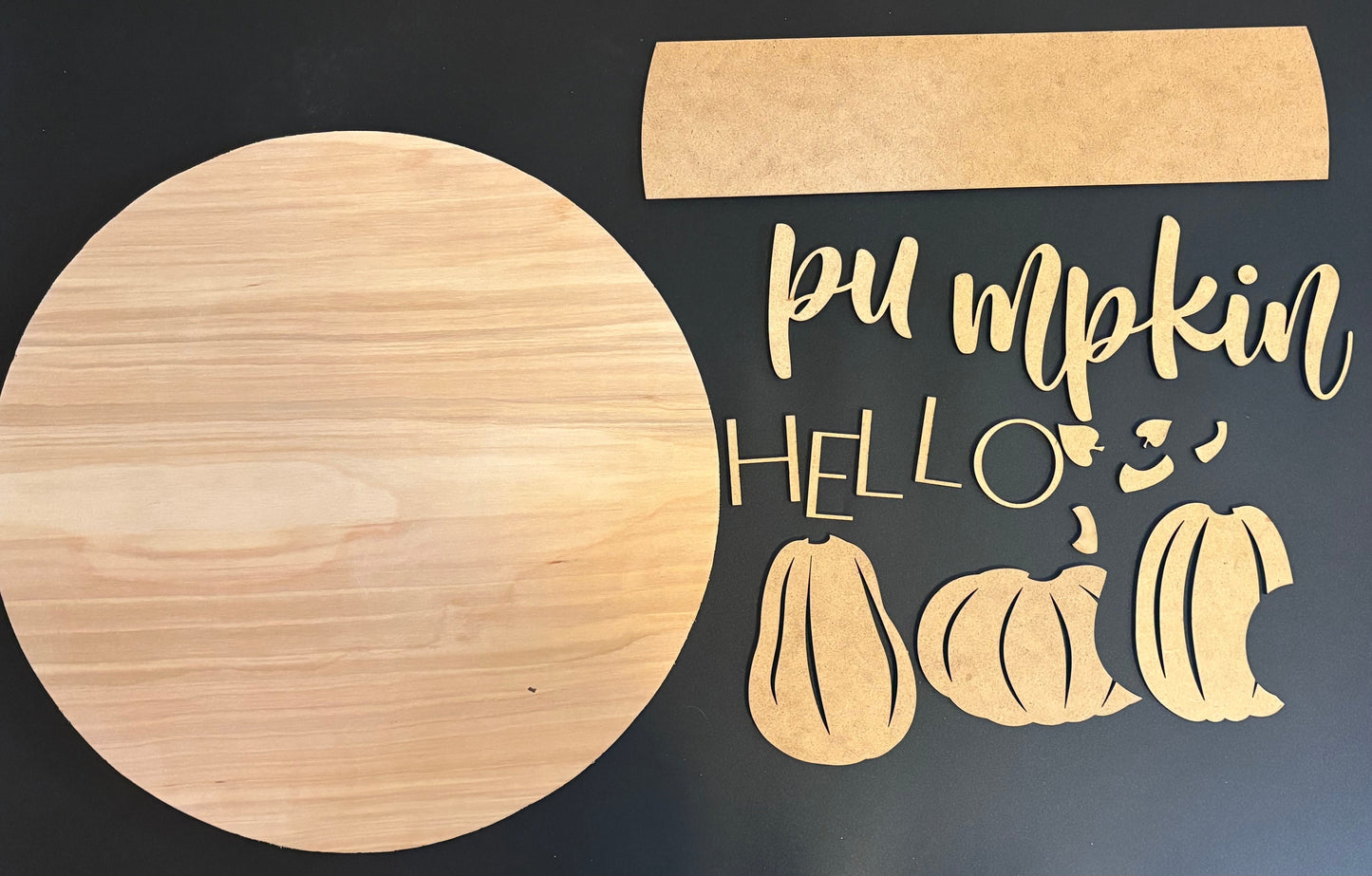 Wooden cutouts of pumpkins and 'Pumpkin Hello' text on a dark background
