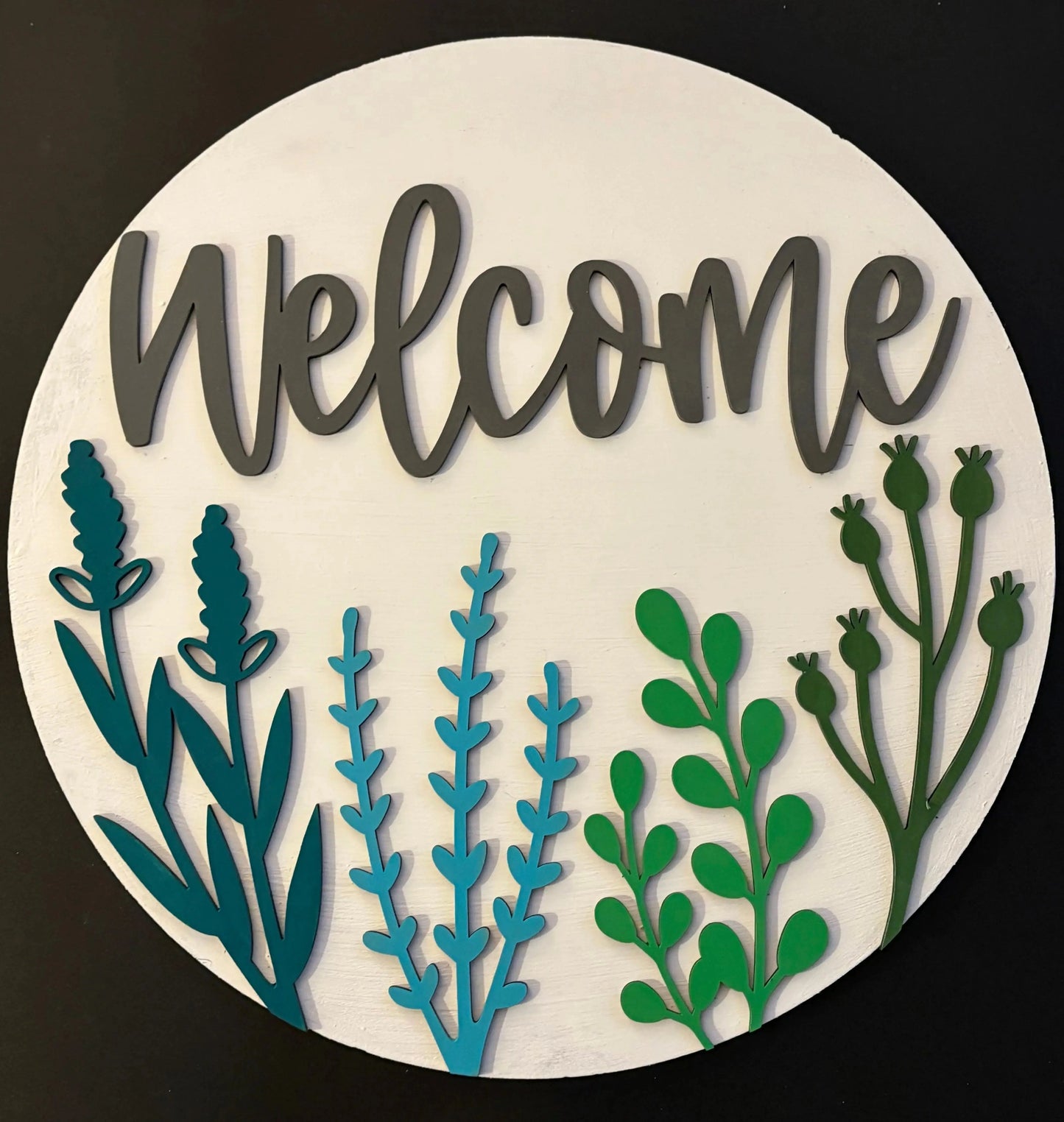 Round wooden sign with 'Welcome' text and green and blue leaf designs on a white background