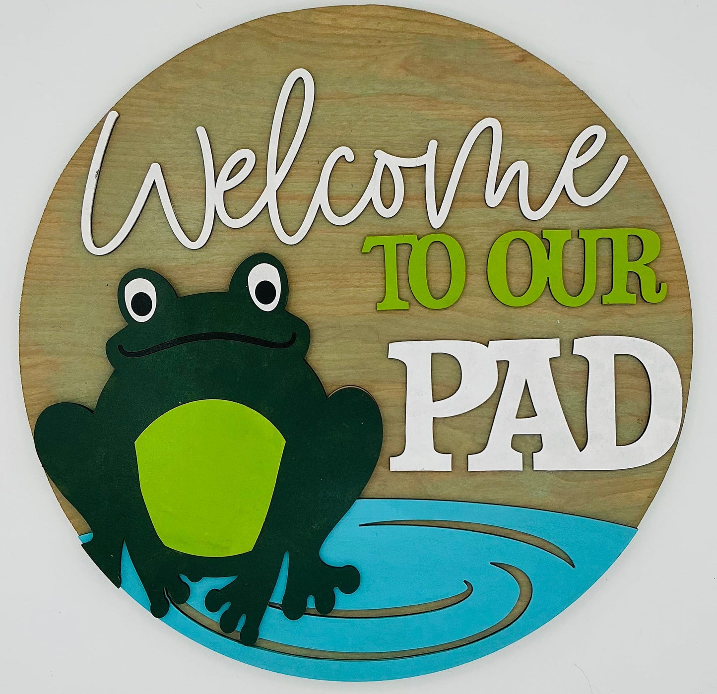 Wooden sign with a frog design and text 'Welcome TO OUR PAD' on a white background