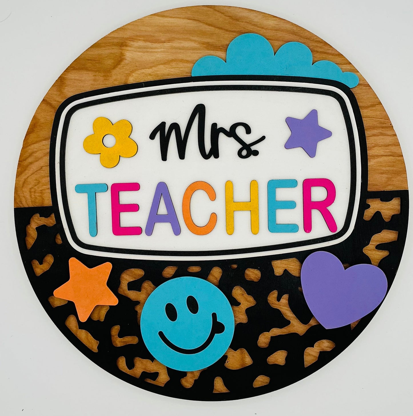 Decorative sign with 'Mrs Teacher' text and colorful graphics on a wooden background