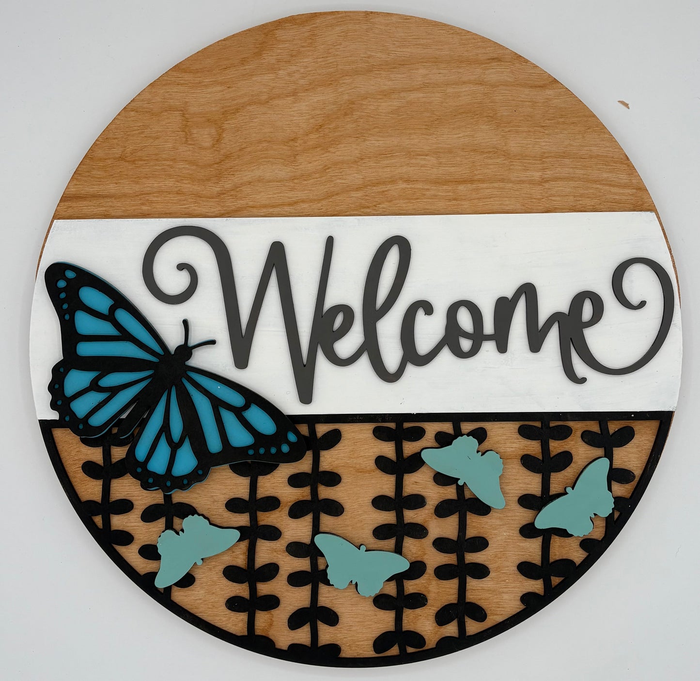 Round wooden sign with 'Welcome' text and blue butterfly design on a white background