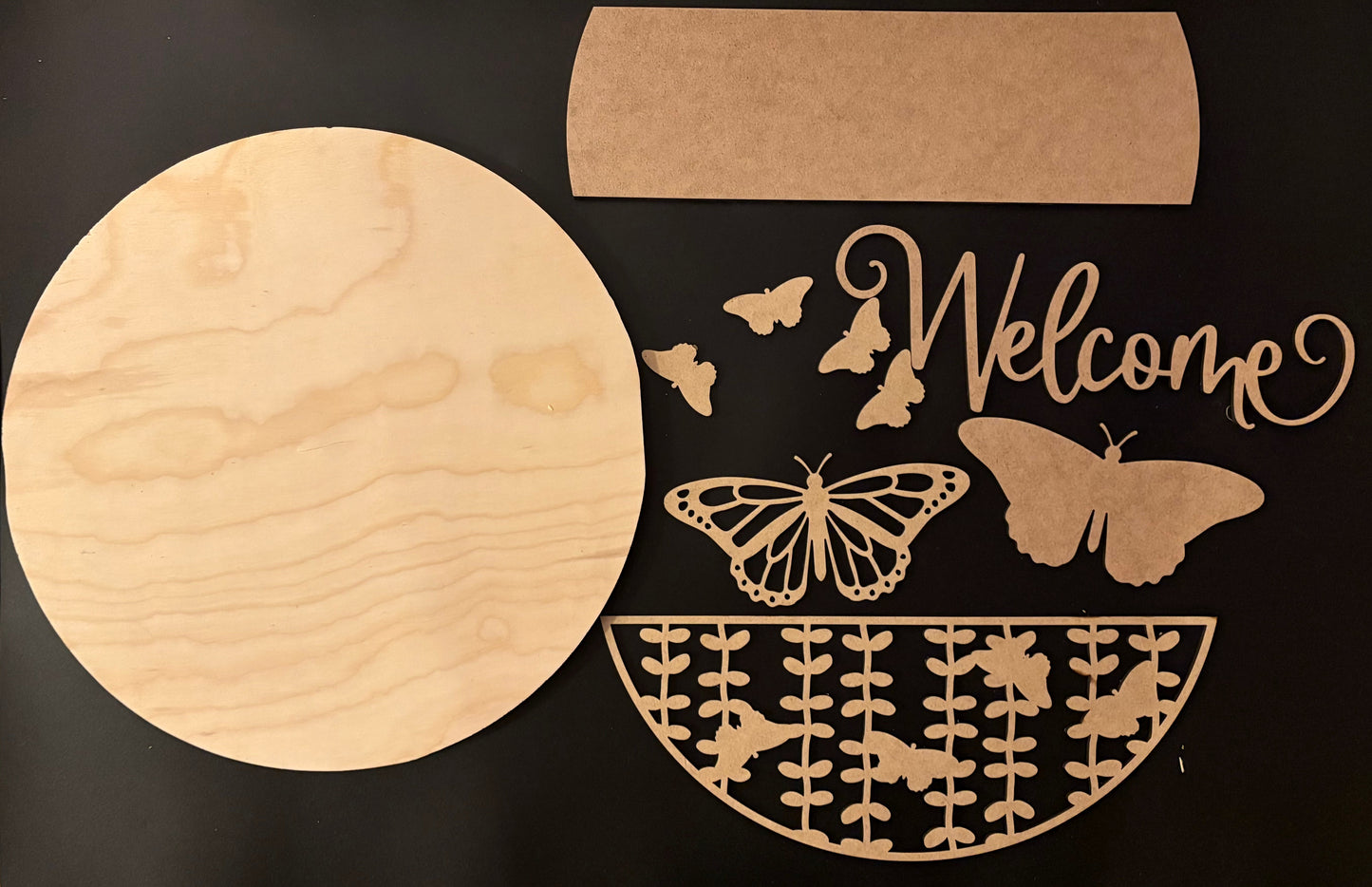 Wooden cutout with 'Welcome' and butterfly designs on a black background