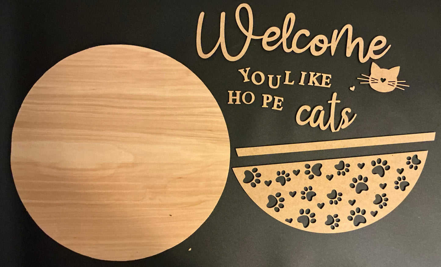 Decorative sign with 'Welcome YOU LIKE HO PE cats' text and paw prints on a black background.