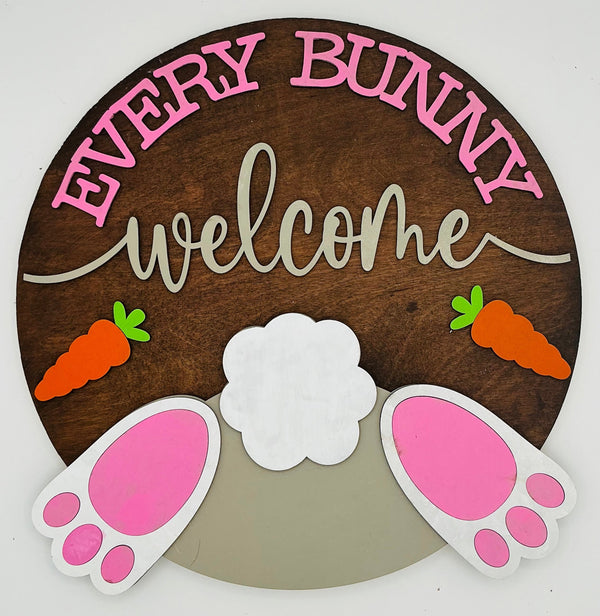 Decorative sign with 'Every Bunny Welcome' text, bunny ears, and carrots on a brown background.