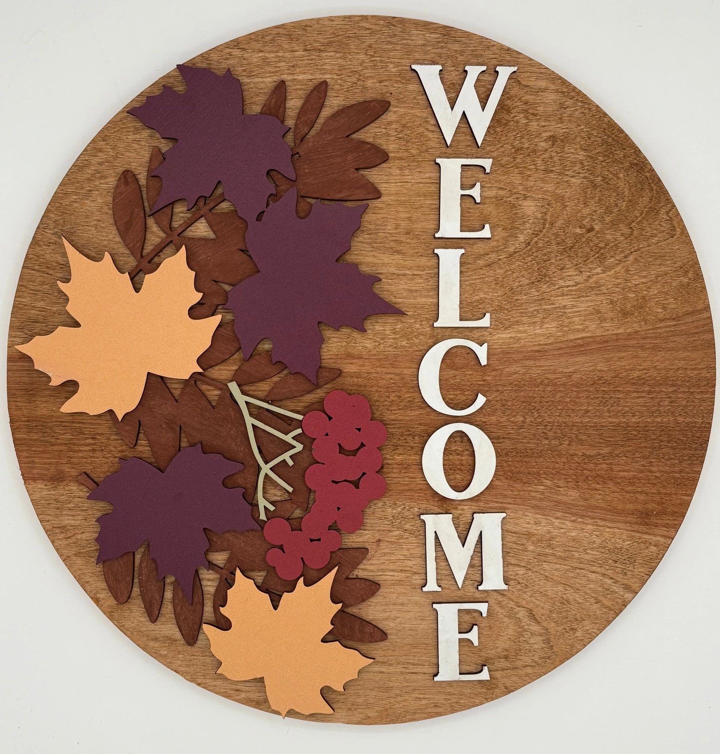 Wooden round sign with autumn leaf designs and 'WELCOME' text on a white background