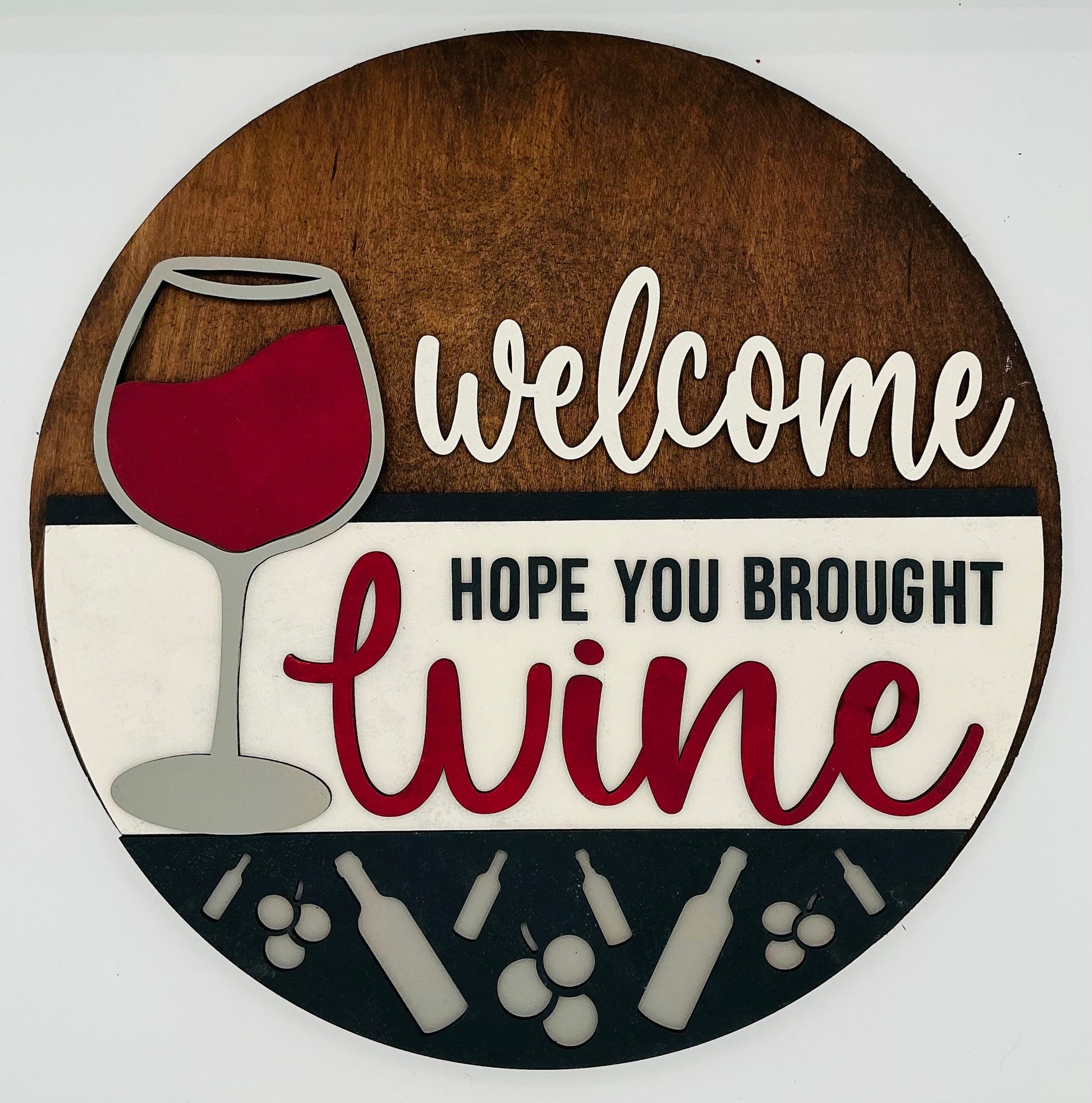 Round wooden sign with a wine glass and text 'Welcome, hope you brought wine' on a white background.
