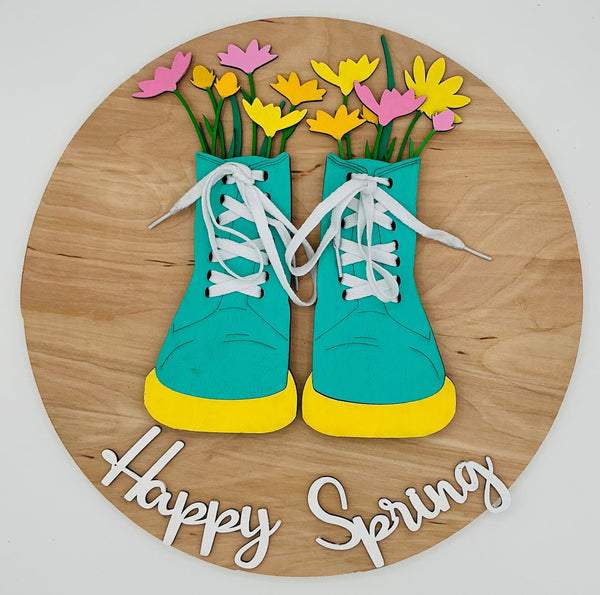 Decorative wall art with turquoise shoes, yellow socks, and flowers on a wooden board with 'Happy Spring' text.