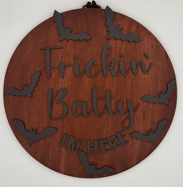 Wooden circular sign with 'Frickin' Batty In Here' text and bat shapes on a white background