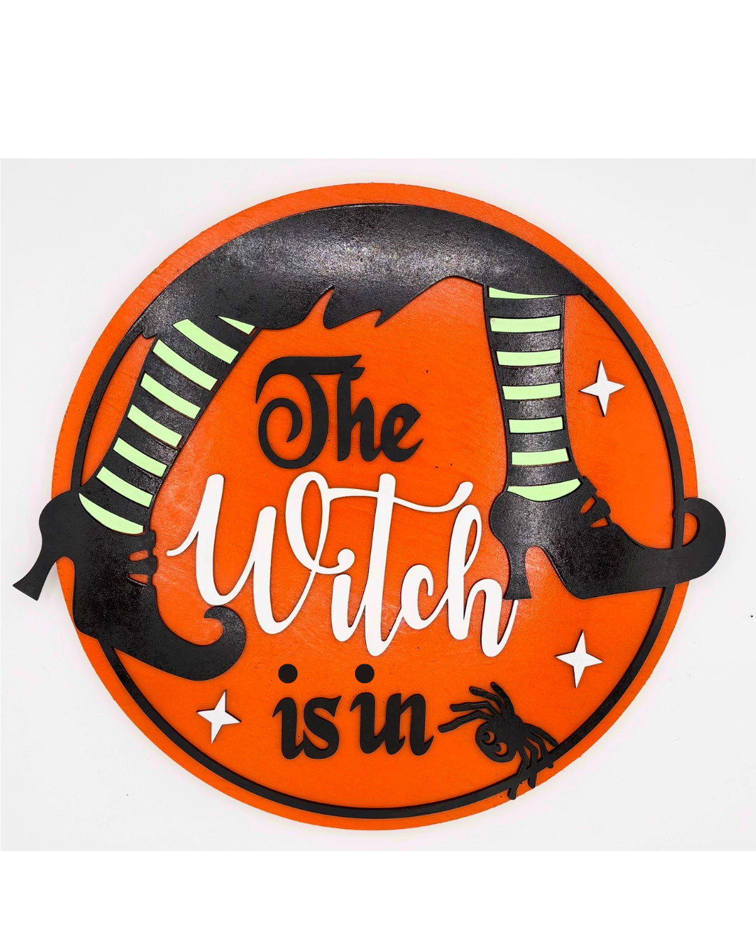 Halloween-themed sign with 'The Witch is in' text and witch legs on an orange background.