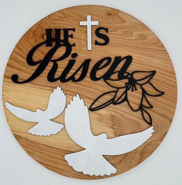 Decorative wood sign featuring 'He is Risen' text, cross, dove silhouettes, and a floral design.