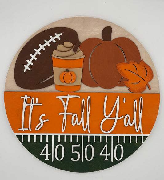 Decorative sign with football, pumpkin, and leaf design on an orange background with 'It's Fall Y'all' text.