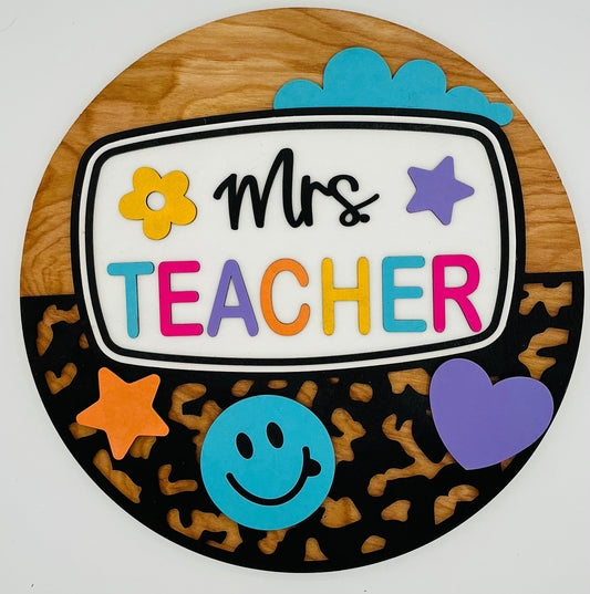 Decorative sign with 'Mrs Teacher' text and colorful graphics on a wooden background