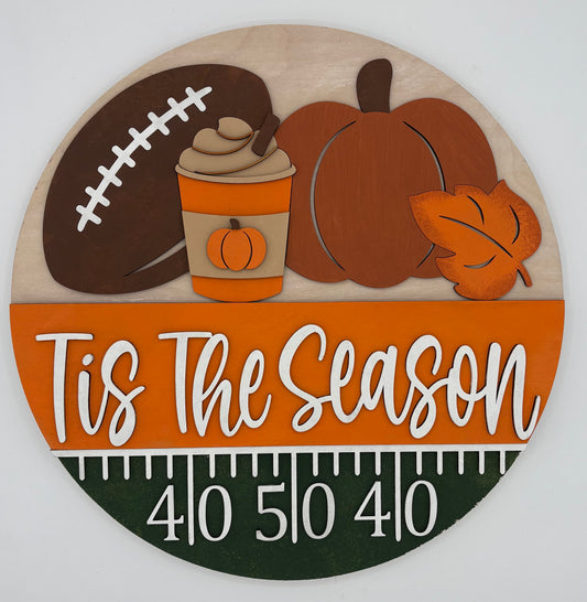 Decorative sign with football, pumpkin, and 'Tis The Season' text on a white background