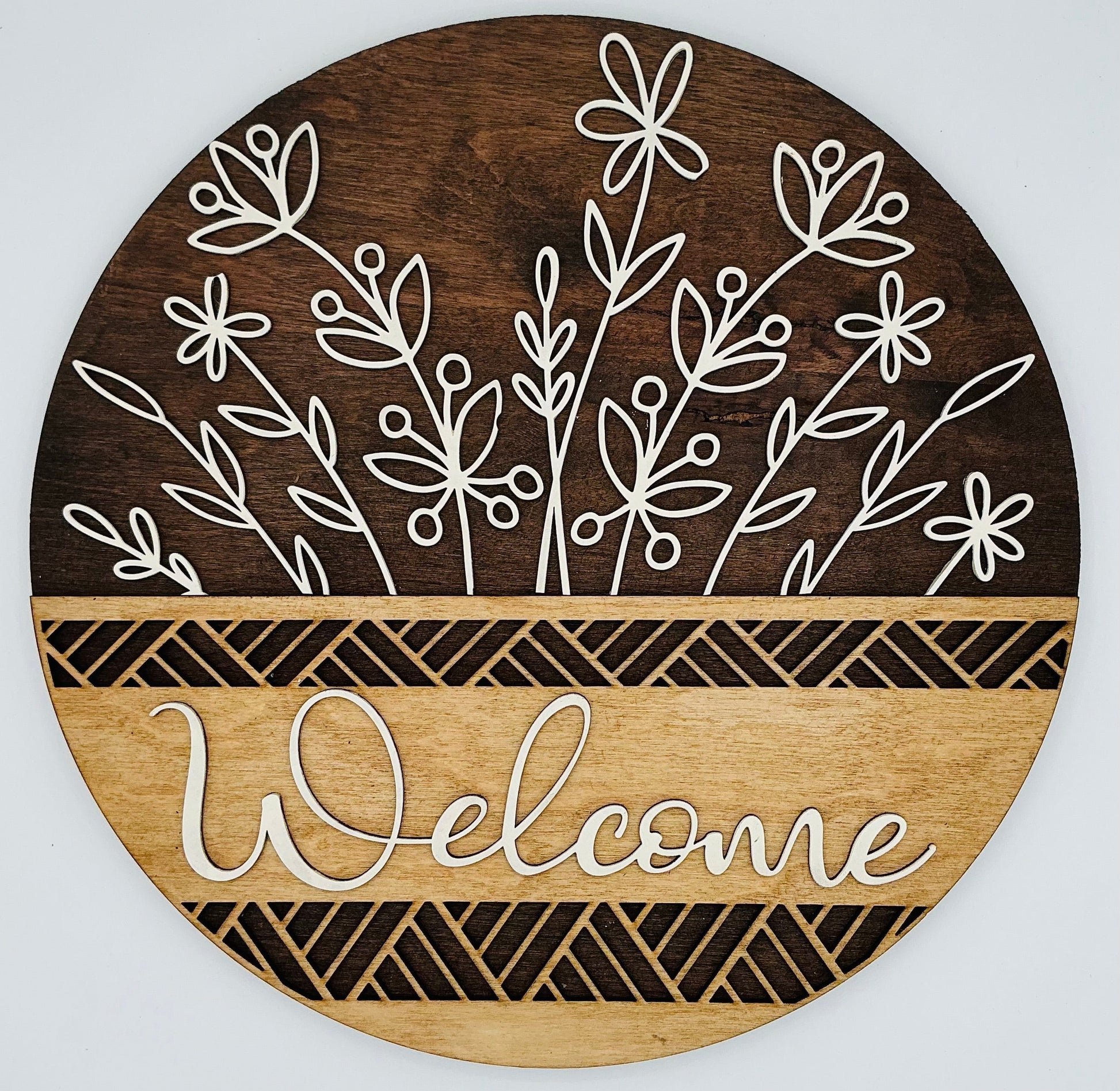 Round wooden sign with white floral designs and 'Welcome' text on a light gray background