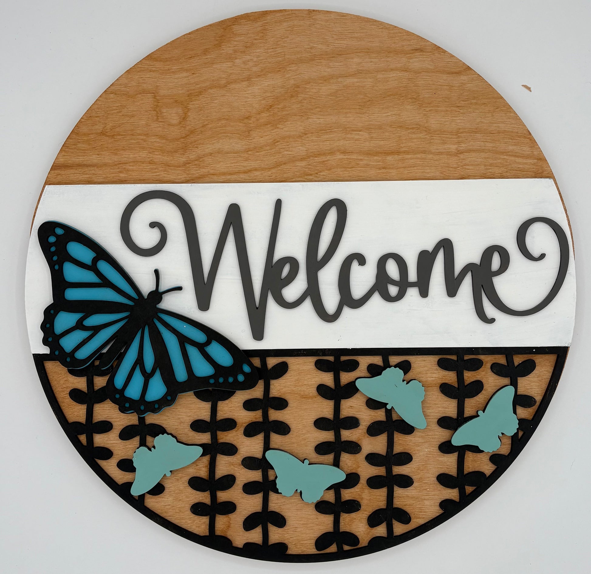 Round wooden sign with 'Welcome' text and blue butterfly design on a white background