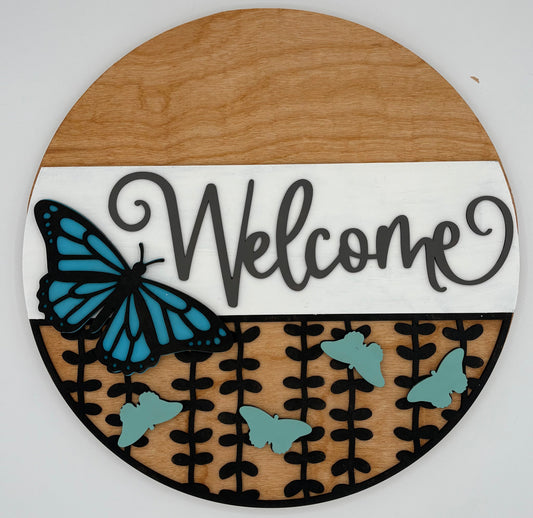 Round wooden sign with 'Welcome' text and blue butterfly design on a white background