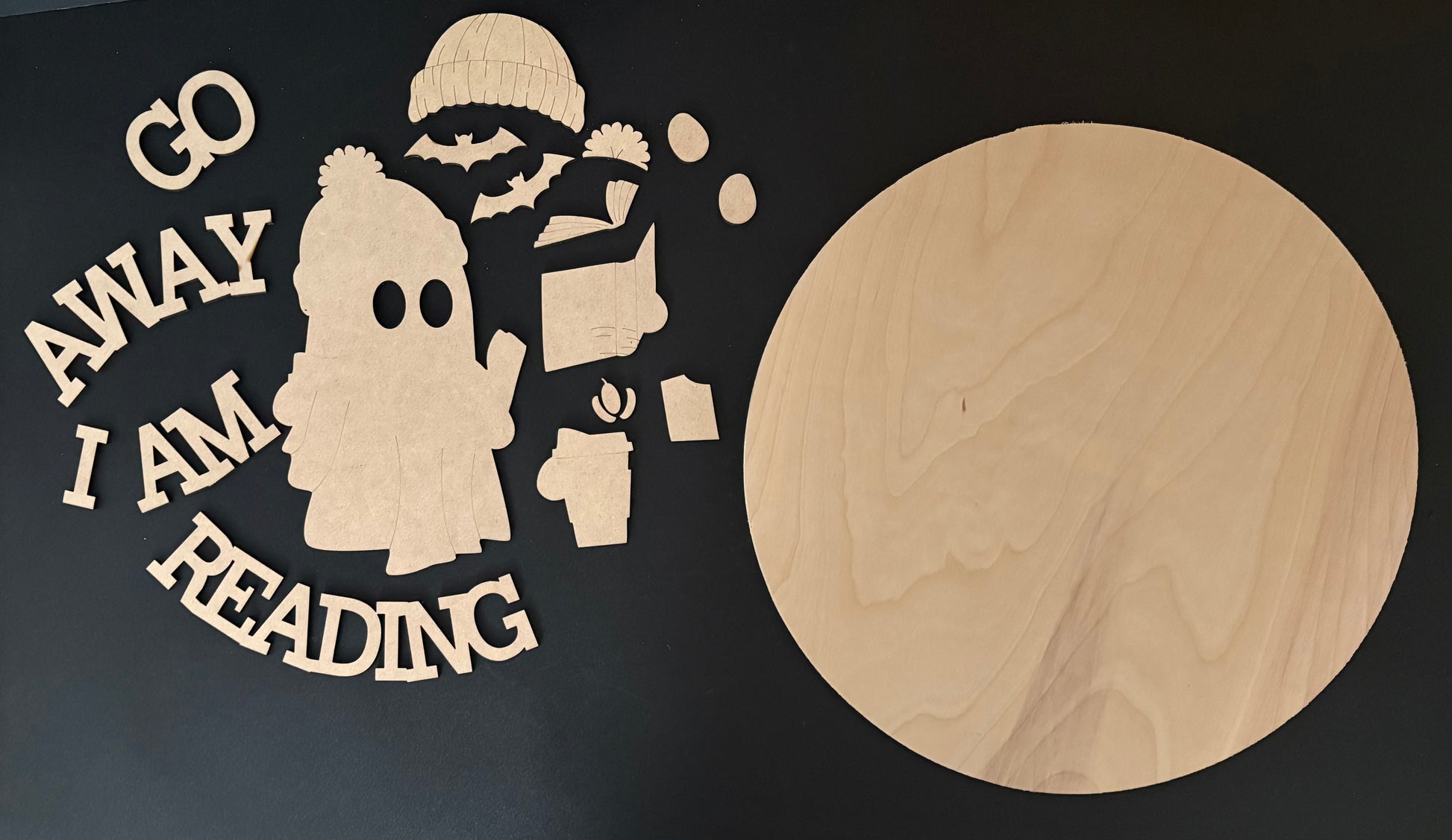Wooden cutout with text 'Go Away I Am Reading' next to a round wooden board on a black background
