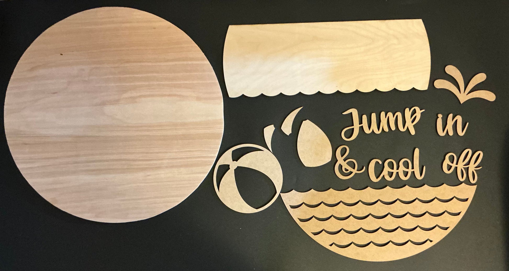 Wooden cutout of a beach scene with 'Jump in & cool off' text on a black background
