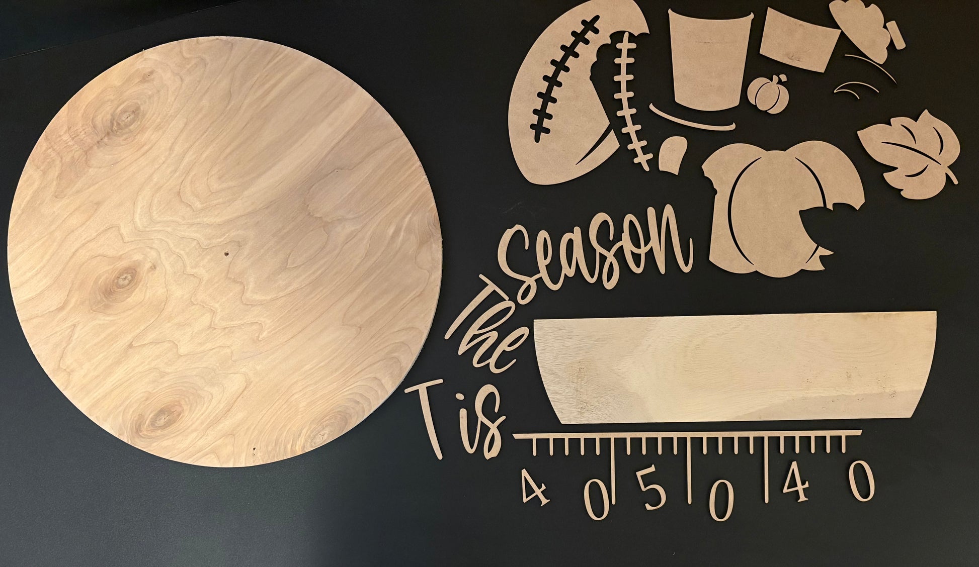 Wooden cutouts with 'Tis the season' text and various shapes on a dark background