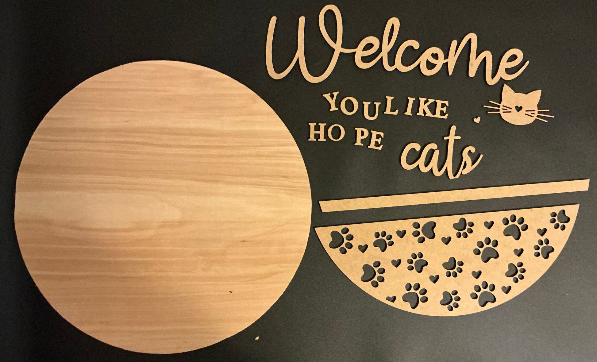Decorative sign with 'Welcome YOU LIKE HO PE cats' text and paw prints on a black background.